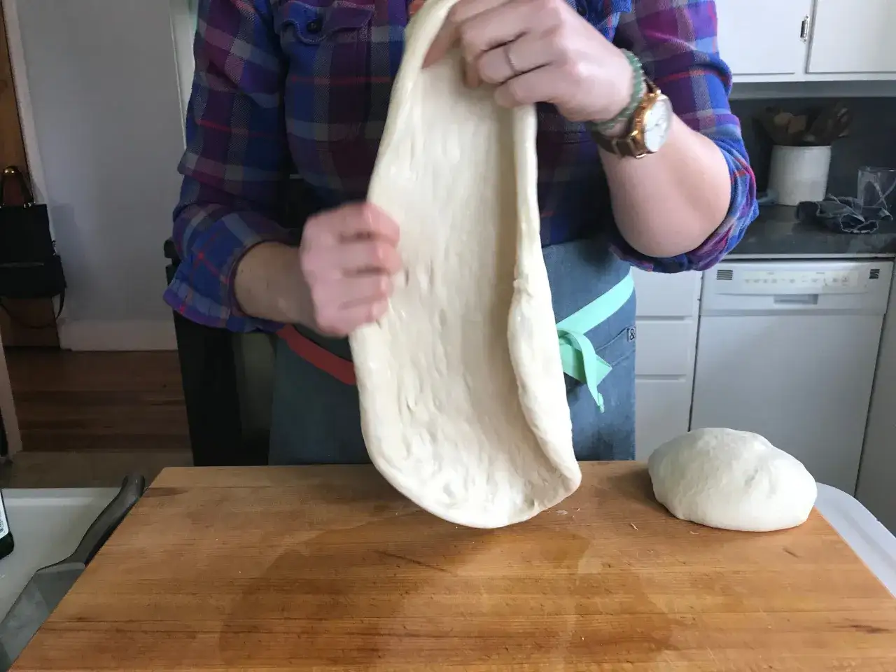 Préparation d'une pâte à pizza fine, étirée à la main sur une planche en bois. Une boule de pâte repose à côté.