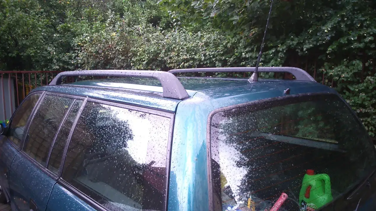 Uszczelka anteny astra h na dachu zielonego kombi, pokrytego kroplami deszczu.