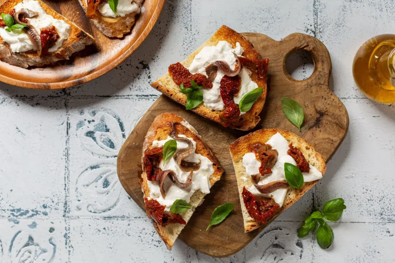 D&eacute;licieuse entr&eacute;e de burrata sur pain grill&eacute;, garnie de tomates s&eacute;ch&eacute;es, d'anchois et de basilic frais. Un d&eacute;lice !