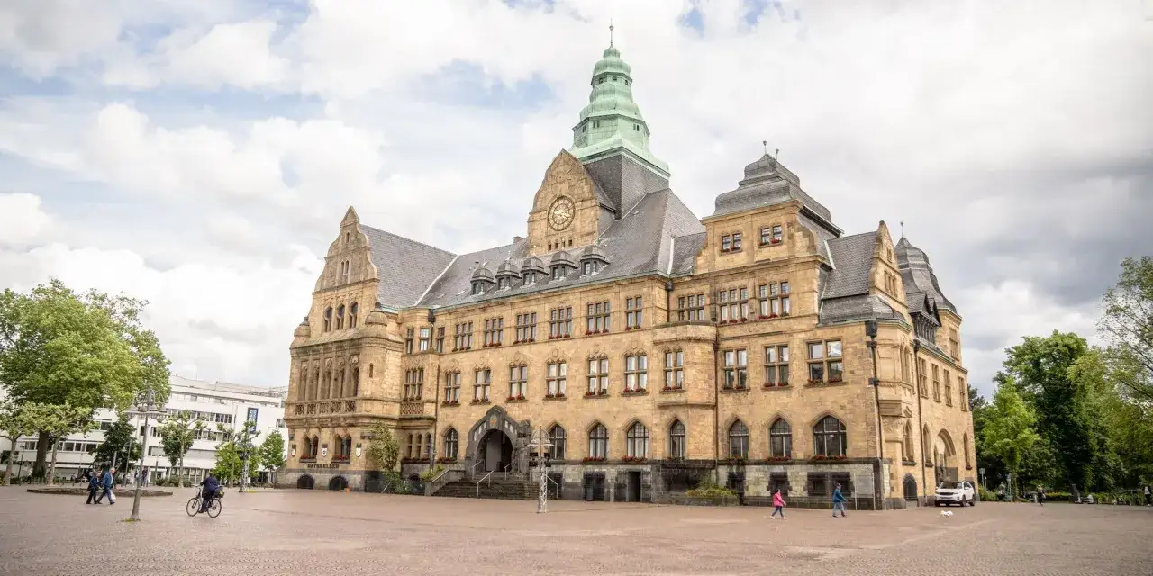 Das Rathaus am Marktplatz Recklinghausen mit seinem markanten Turm und der Sandsteinfassade. Menschen spazieren über den Platz.