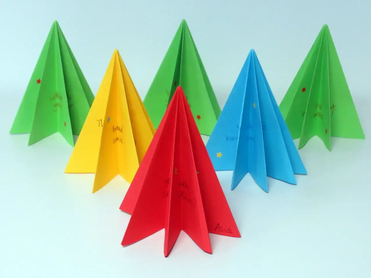 Kolorowe choinki origami płaskie z życzeniami. Zielone, żółte, czerwone i niebieskie drzewka ozdobione gwiazdkami.