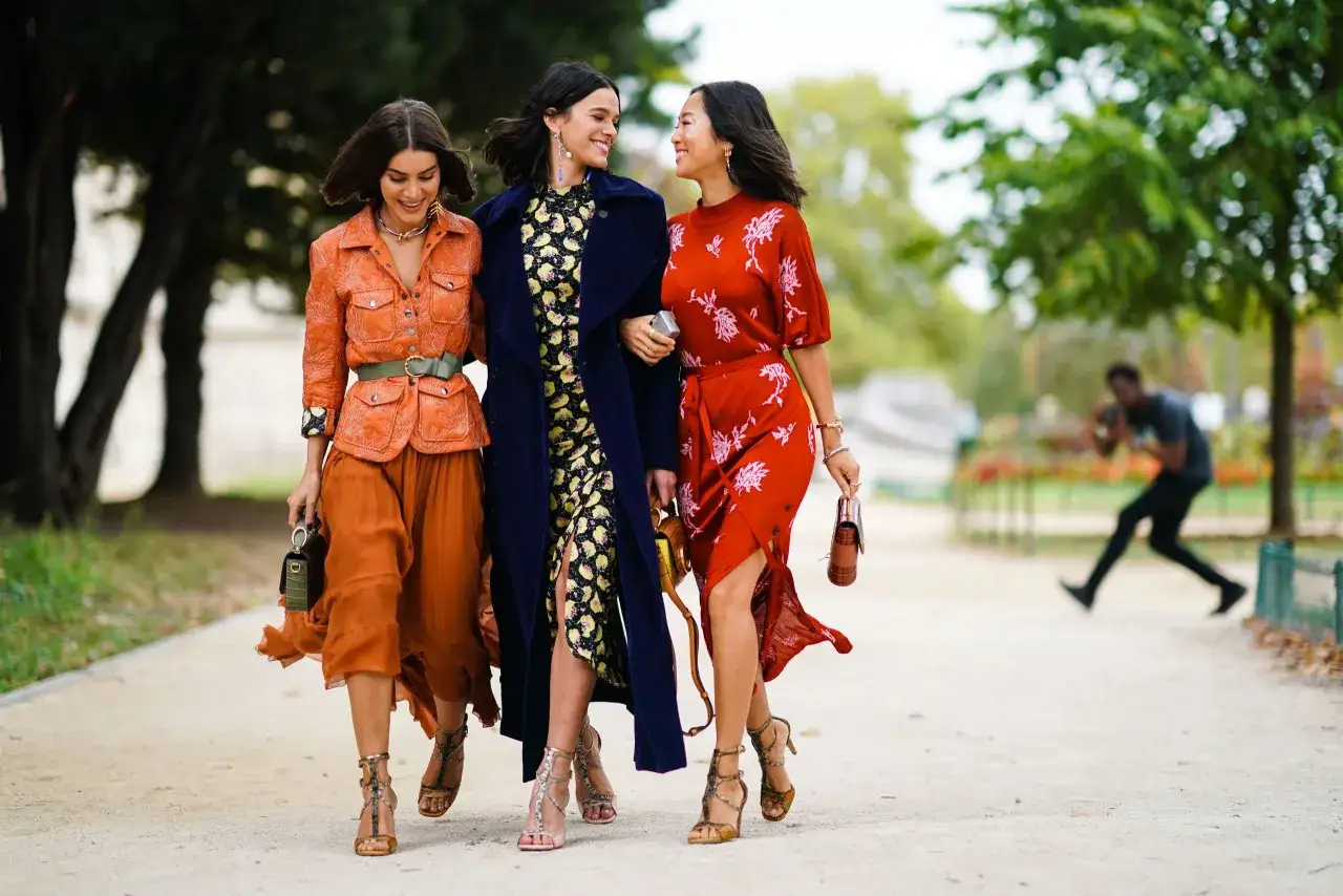 Tre amiche passeggiano, ognuna con un outfit perfetto per uscire con un ragazzo: arancione, floreale e rosso.