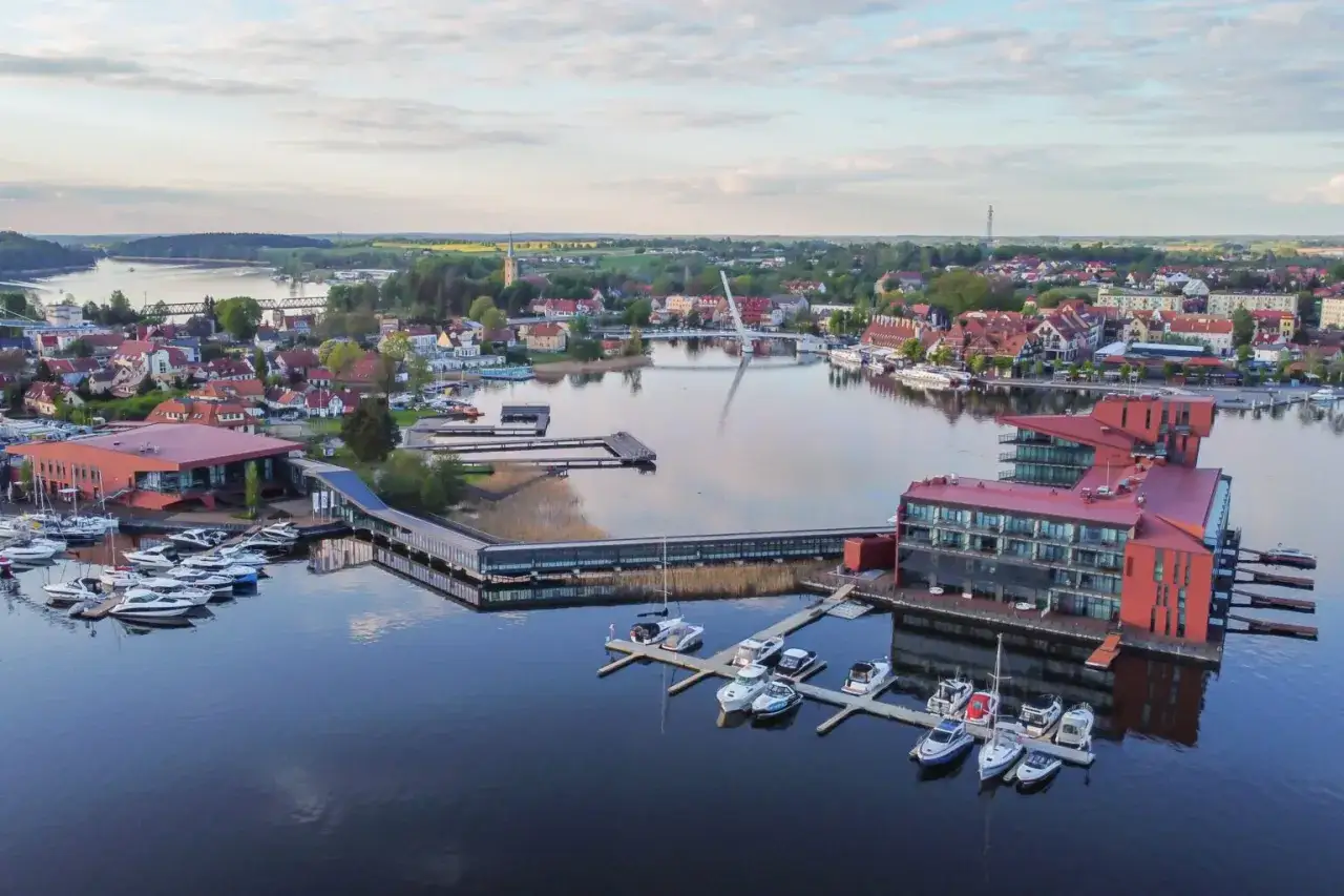 Widok na nowoczesny hotel i przystań z łodziami na jeziorze. To jedno z najpiękniejszych miejsc w Polsce, Mazury.