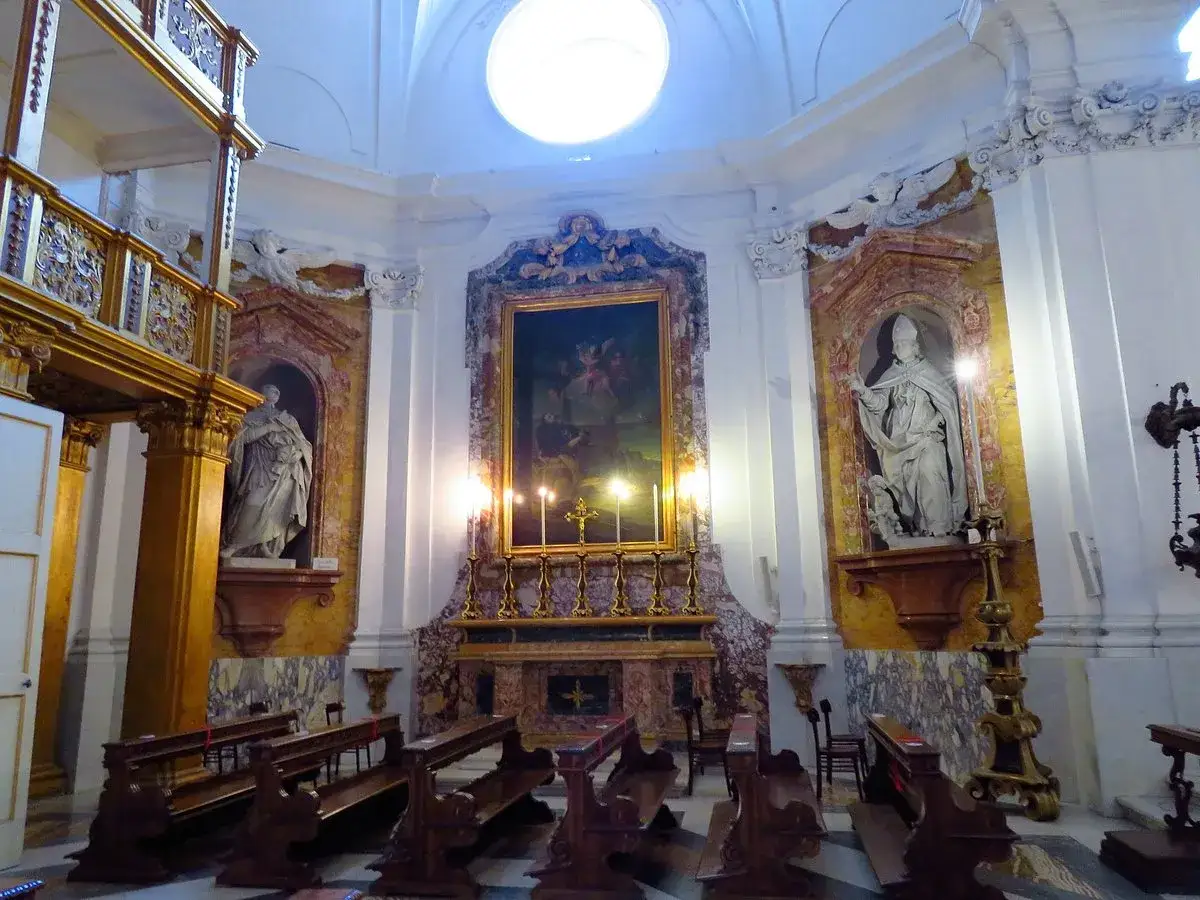 Interno della cappella reale a Portici: statue, dipinto sull'altare, candelabri e panche di legno.