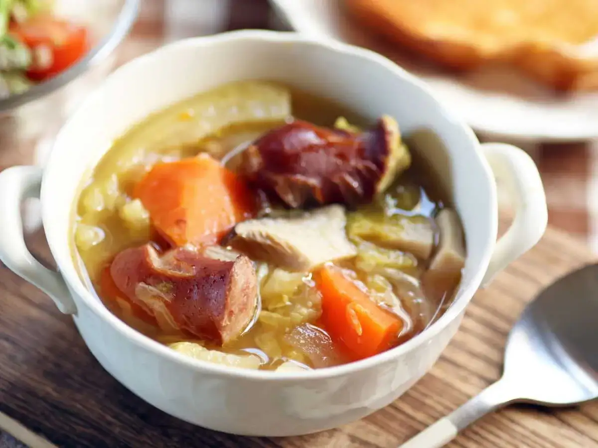 Un réconfortant plat de potee au chou, avec des morceaux de saucisse fumée, carottes et chou dans un bouillon savoureux.