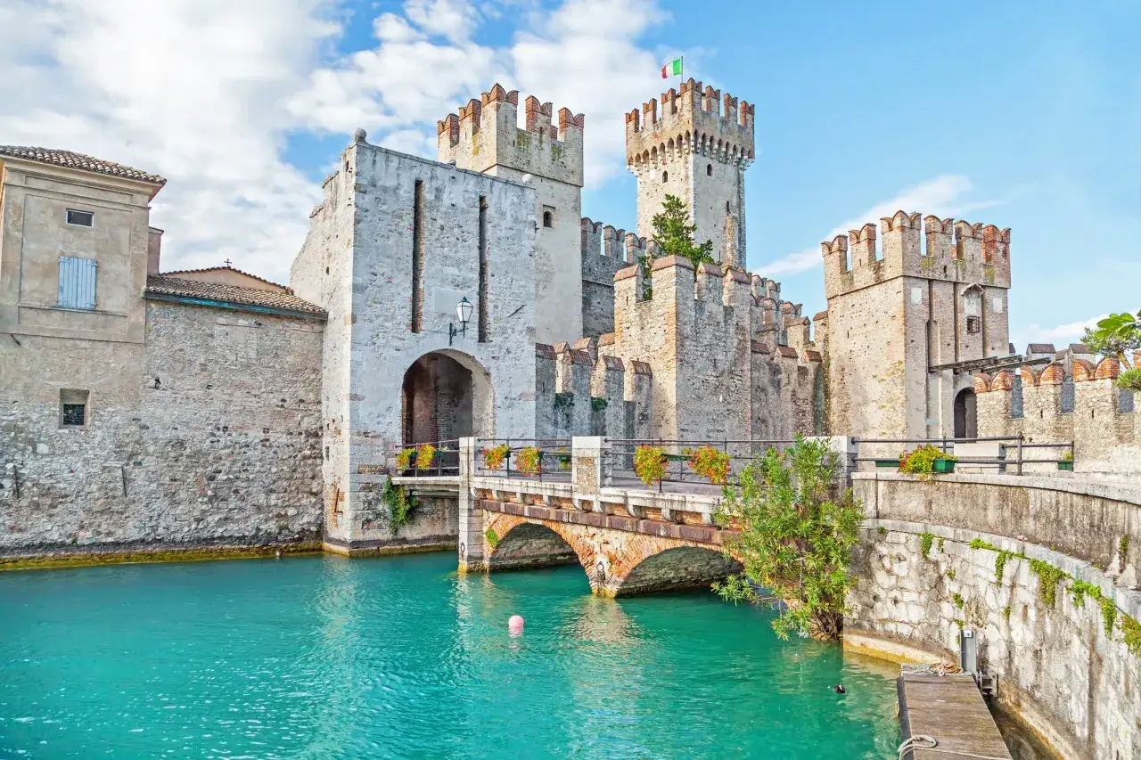 Il Sirmione castello, con le sue torri merlate e il ponte ad arco, si specchia nelle acque turchesi del lago.
