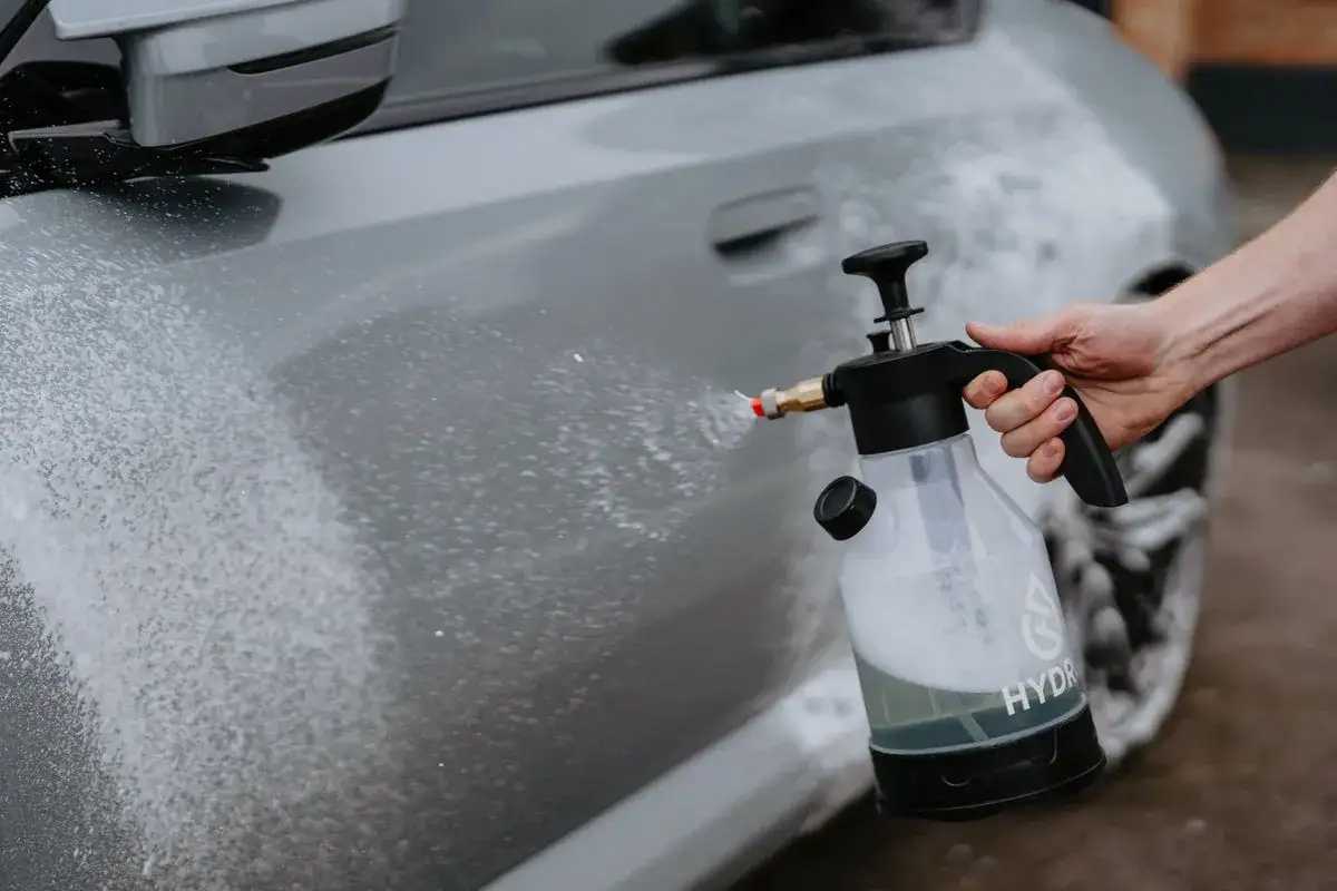 En hand h&aring;ller en tryckspruta med skum som sprutas mot en gr&aring; bil. Sprayflaskor &auml;r bra f&ouml;r bilv&aring;rd.