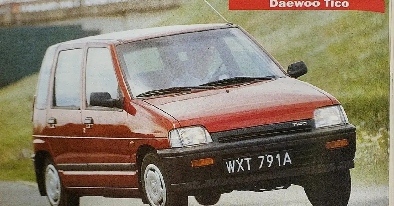 Czerwony Daewoo Tico z tablicą rejestracyjną WXT 791A jedzie po drodze wśród zieleni.