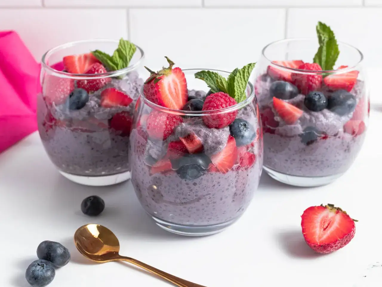 Trois coupes de pudding aux graines de chia, garnies de baies fraîches et de menthe. Un délice sain pour profiter du graine de chia bienfait.