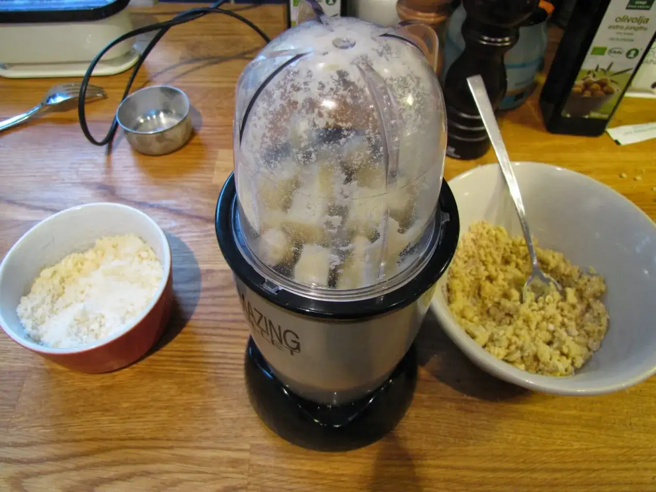 F&ouml;rbereder ingredienser f&ouml;r ett basilika recept. En mixer med bananbitar st&aring;r bredvid sk&aring;lar med mj&ouml;l och en f&auml;rdigblandad smet.