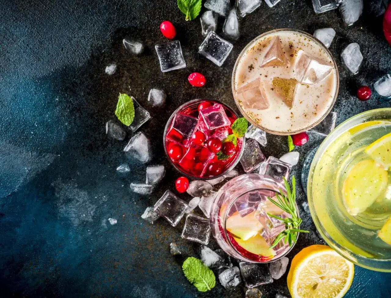 Erfrischende Cocktails, darunter ein Greyhound, mit Eis, Minze und Beeren auf dunklem Hintergrund.