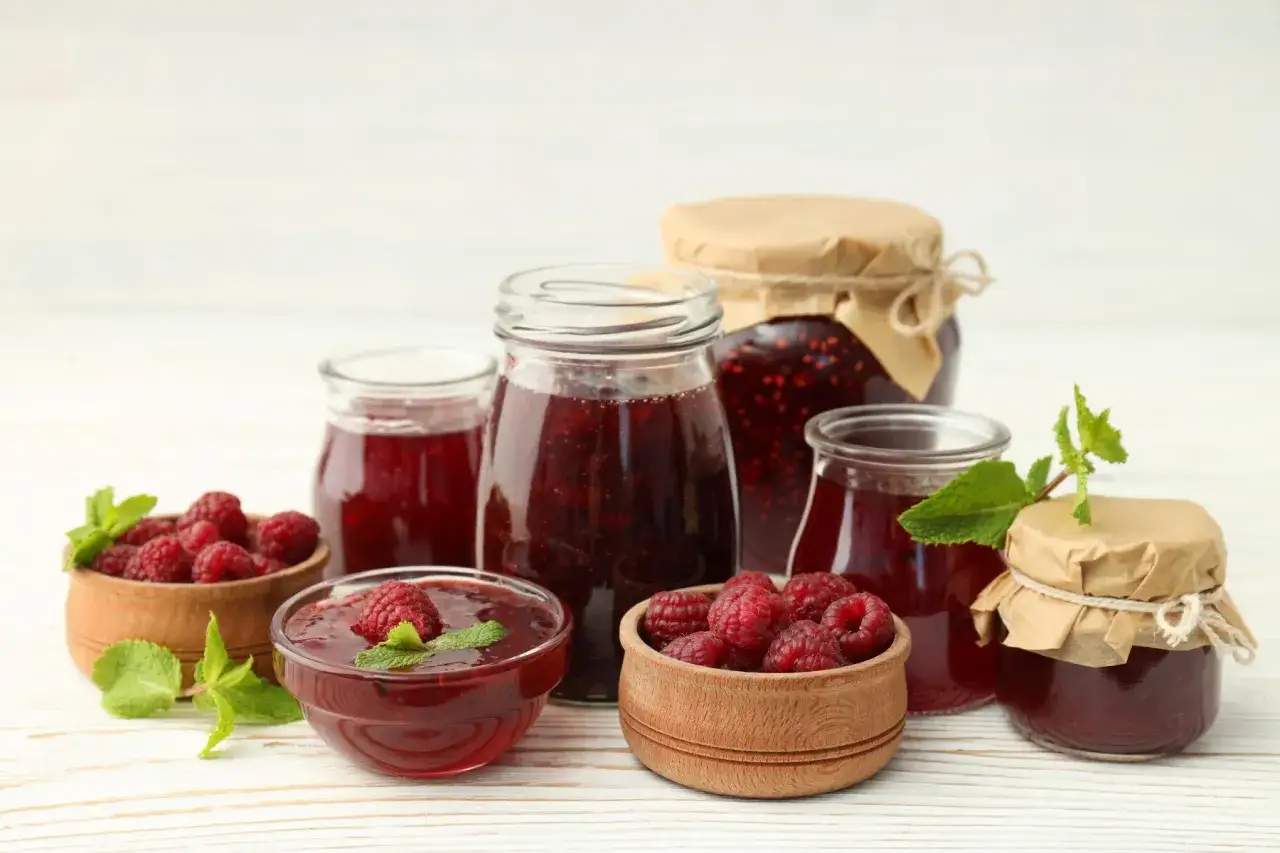 Słoiki z domowym dżemem malinowym i świeże maliny w drewnianych miseczkach. Pyszny sok z malin czeka na degustację.