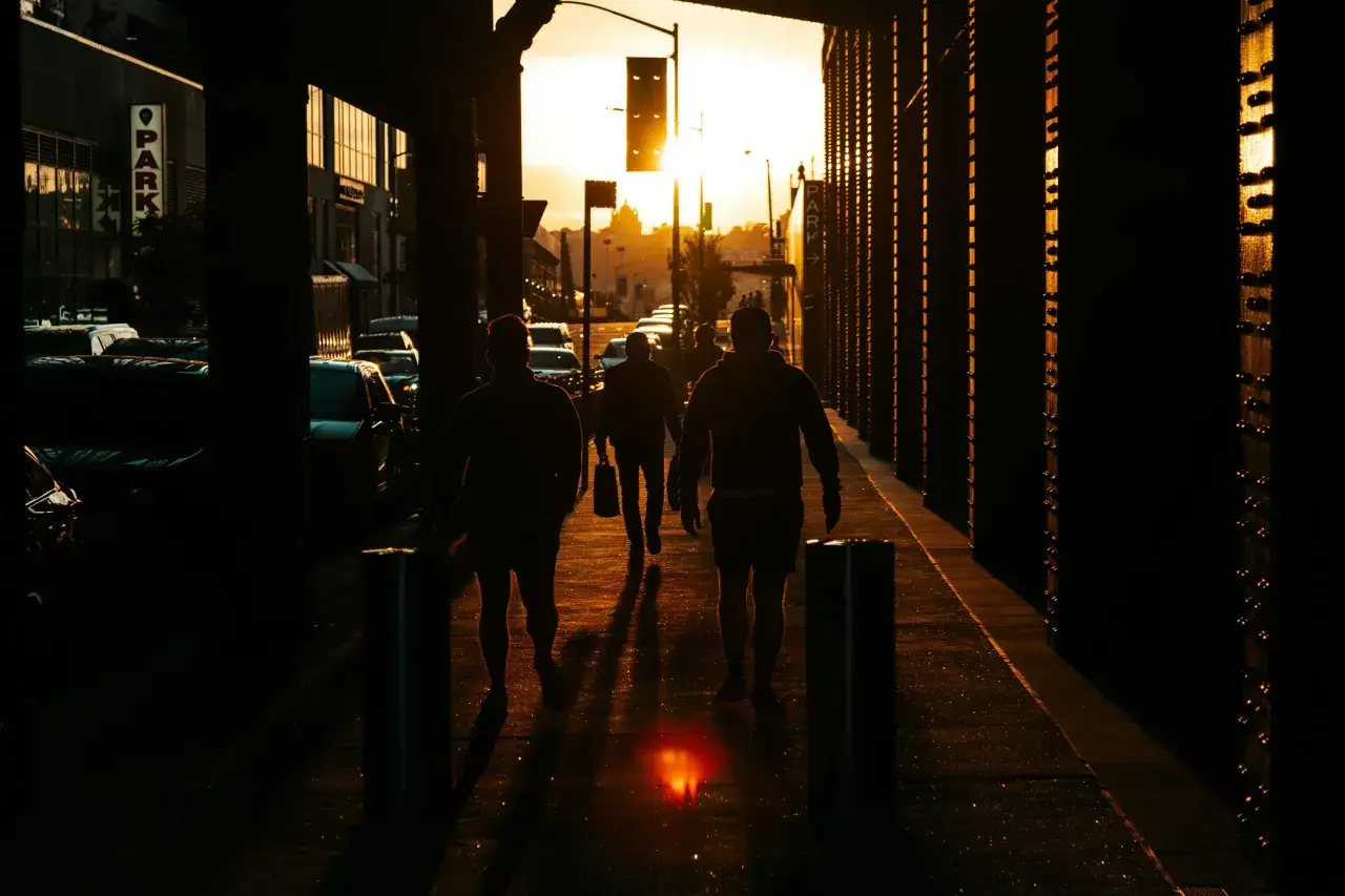 Silhouettes di persone camminano su un marciapiede illuminato da un tramonto dorato. Una **foto da fare al tramonto** perfetta per catturare l'atmosfera urbana.