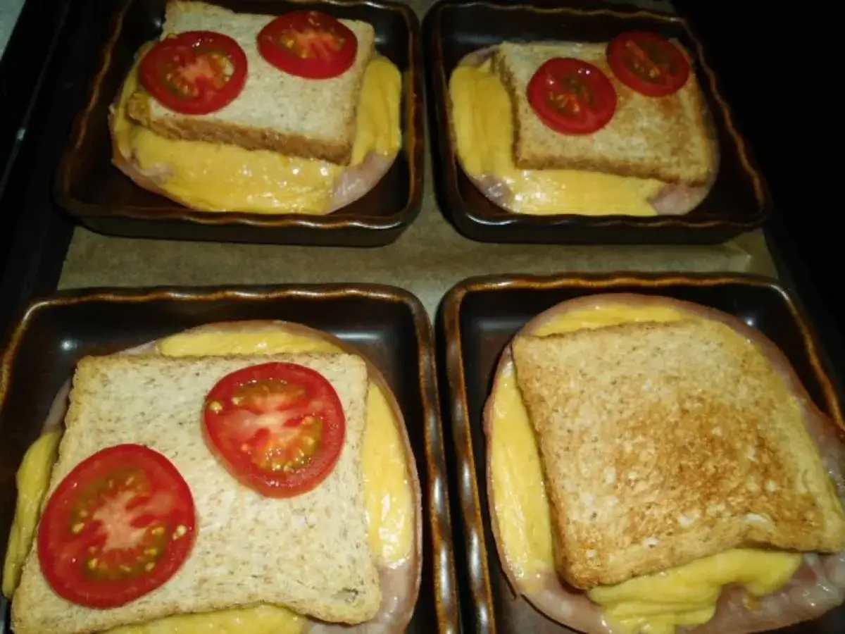 Vier kleine Auflaufformen mit Schinken, K&auml;se, Toast und Tomatenscheiben, bereit f&uuml;r den Toast im Backofen.