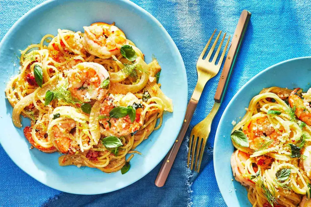 En tallrik med scampi recept: spaghetti med saftiga scampi, toppad med färska örter och parmesan. Två gyllene gafflar ligger redo.