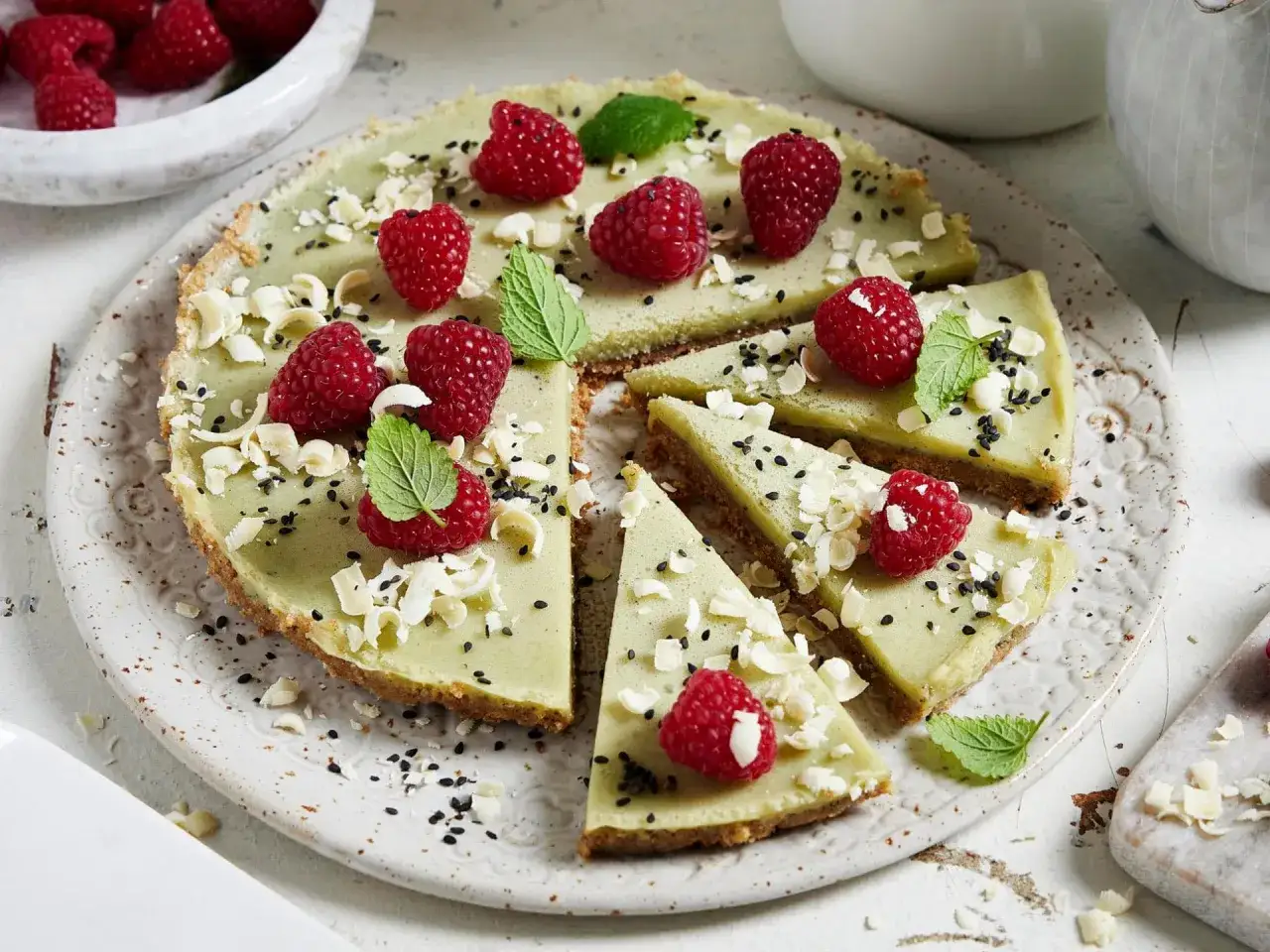 Ein köstlicher Matcha Kuchen, dekoriert mit frischen Himbeeren, weißen Schokostückchen und schwarzen Sesamkörnern.