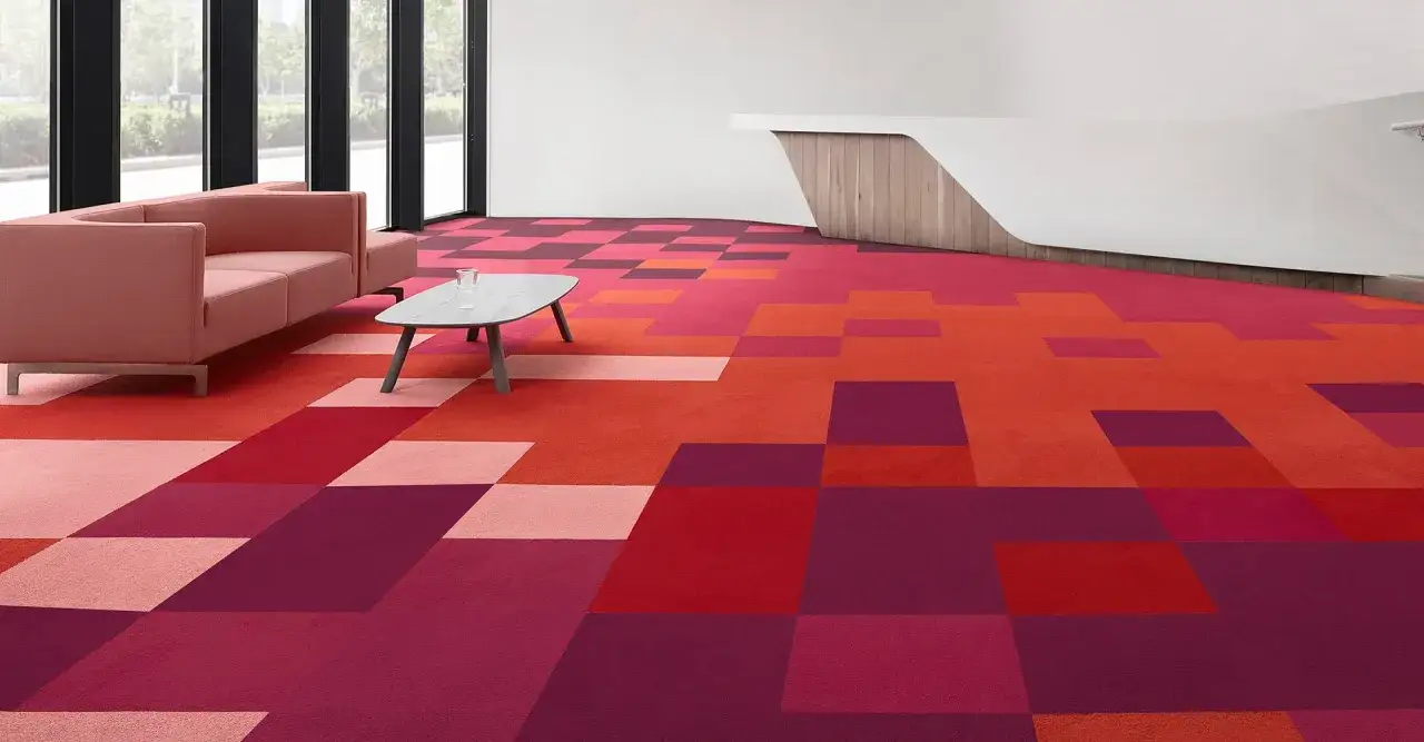 Un ufficio moderno con una moquette a motivi geometrici nei toni del rosso e del rosa. Divano rosa e tavolino grigio.
