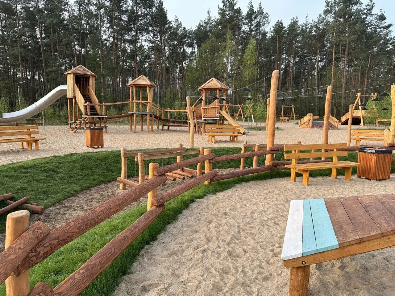 Piaskowy plac zabaw w lesie, pełen drewnianych konstrukcji, zjeżdżalni i huśtawek. Idealne gniezno atrakcje dla dzieci.