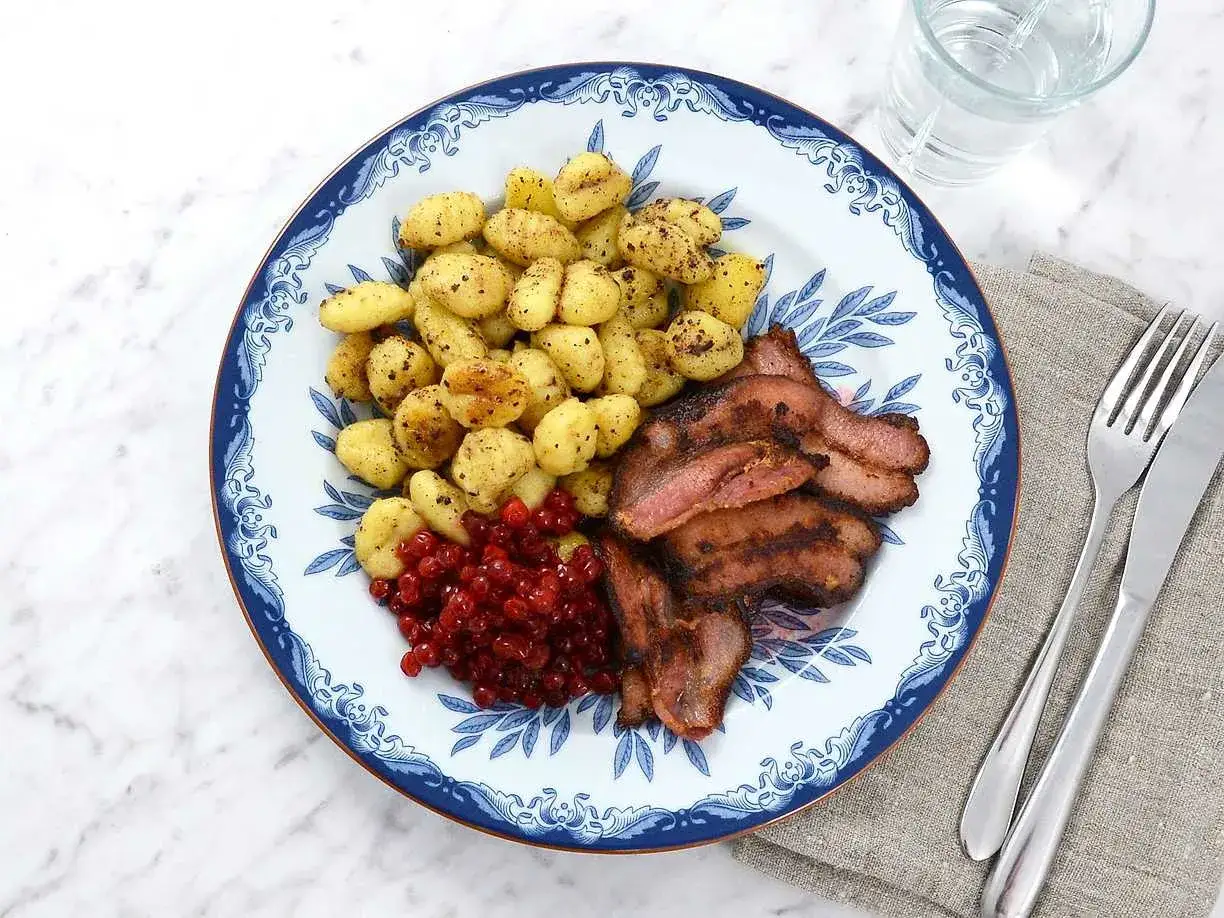 Tallrik med stekt fl&auml;sk, kokt potatis och r&aring;r&ouml;rda lingon. Ett klassiskt svenskt kroppkakor recept.