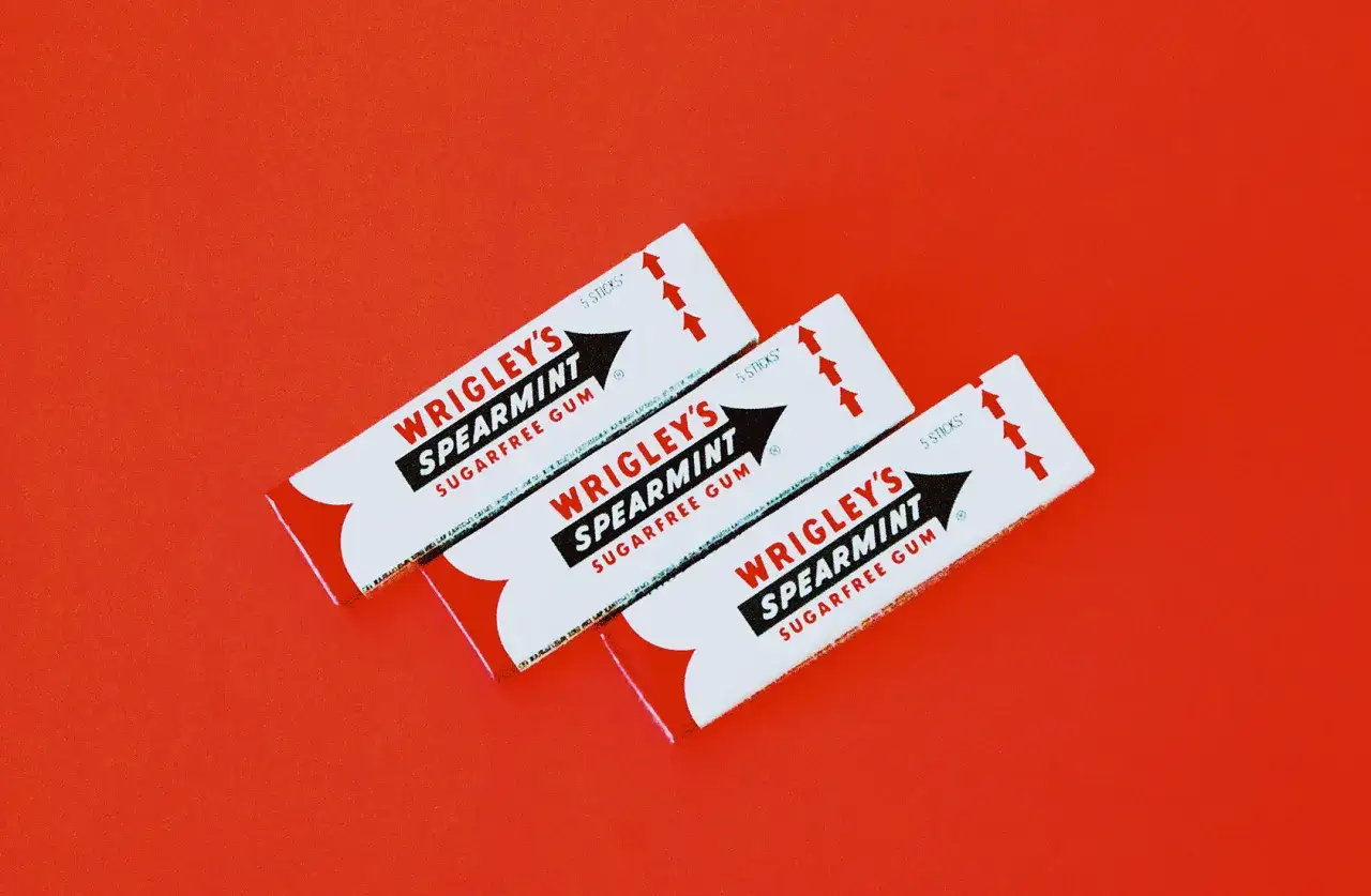 Trzy paczki gumy Wrigley's Spearmint na czerwonym tle. Czy żucie gumy jest zdrowe? Ta bezcukrowa guma może pomóc.