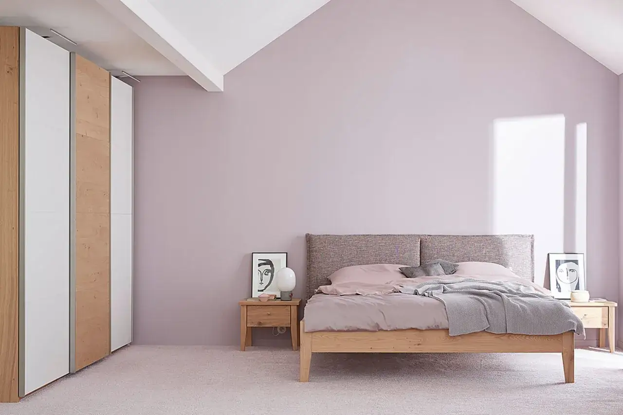 Ein gemütliches Schlafzimmer mit einem Queensize-Bett, das größer ist als ein Standard-Doppelbett. Daneben ein Nachttisch mit Lampe und Bild.
