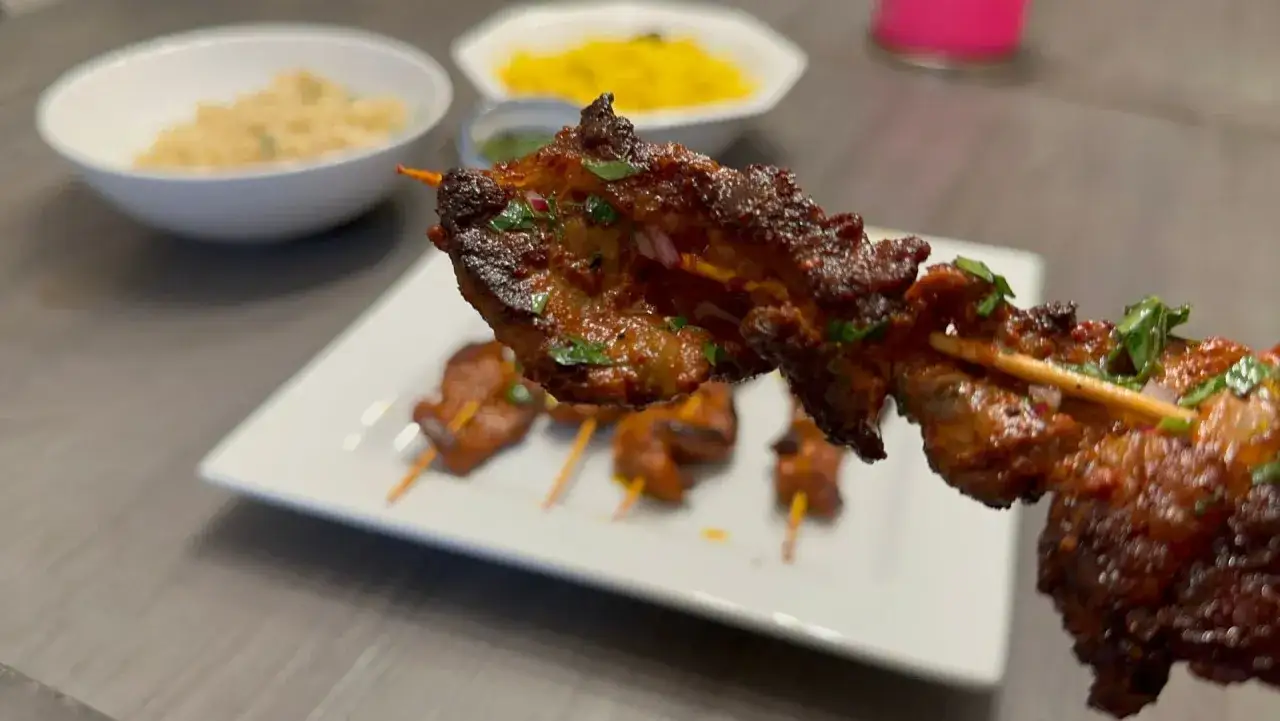 Brochettes de viande marinées, servies avec du riz et une sauce verte. La viande, riche en saveurs, pourrait être sublimée par une touche de crème d'ail.
