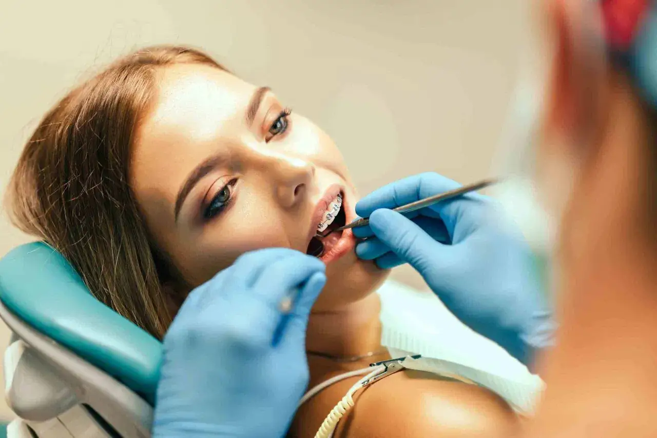 Młoda kobieta z aparatem ortodontycznym u dentysty. Specjalista bada jej jamę ustną, by wykluczyć choroby błony śluzowej.