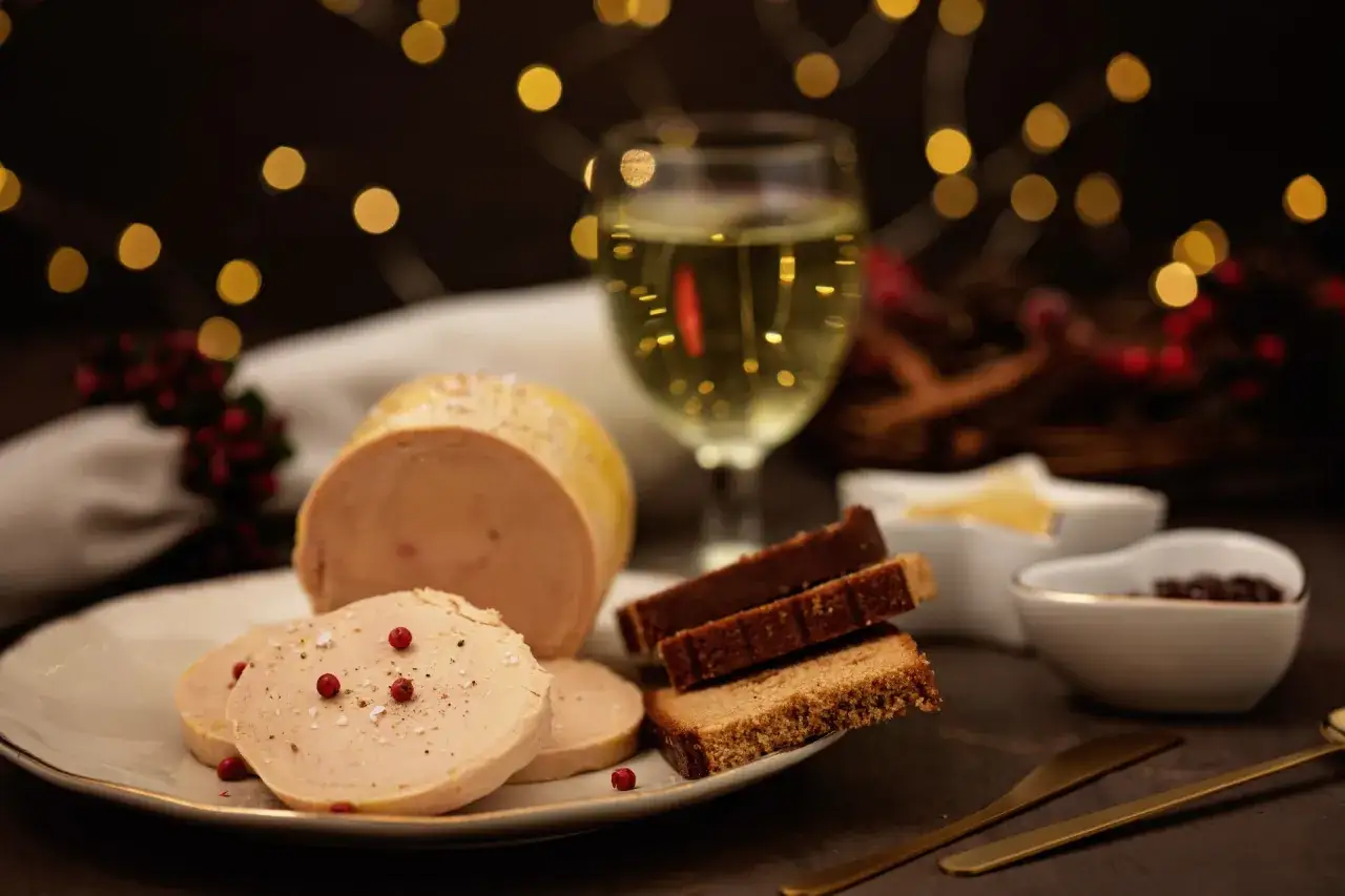 Tranche de vin foie gras sur une assiette, avec du pain d'épices et des baies rouges. Lumières de Noël en arrière-plan.