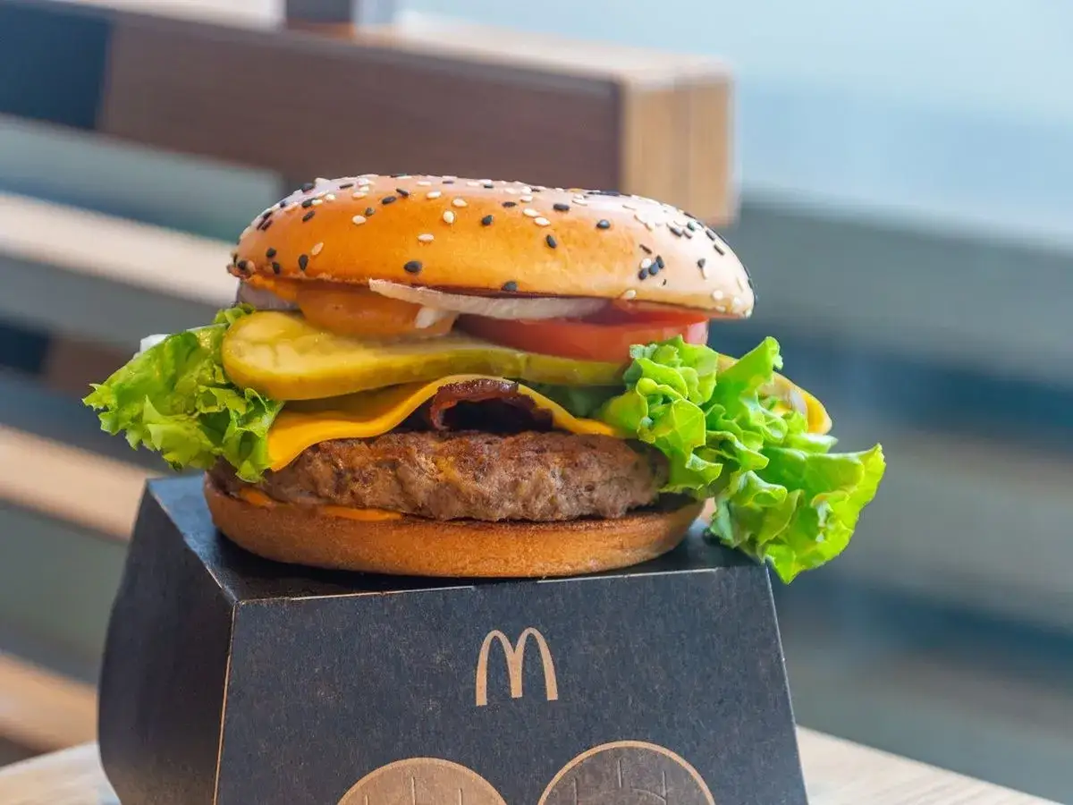 Maestro burger McDonald's z soczystą wołowiną, serem, chrupiącą sałatą i piklami na czarnej tacce.