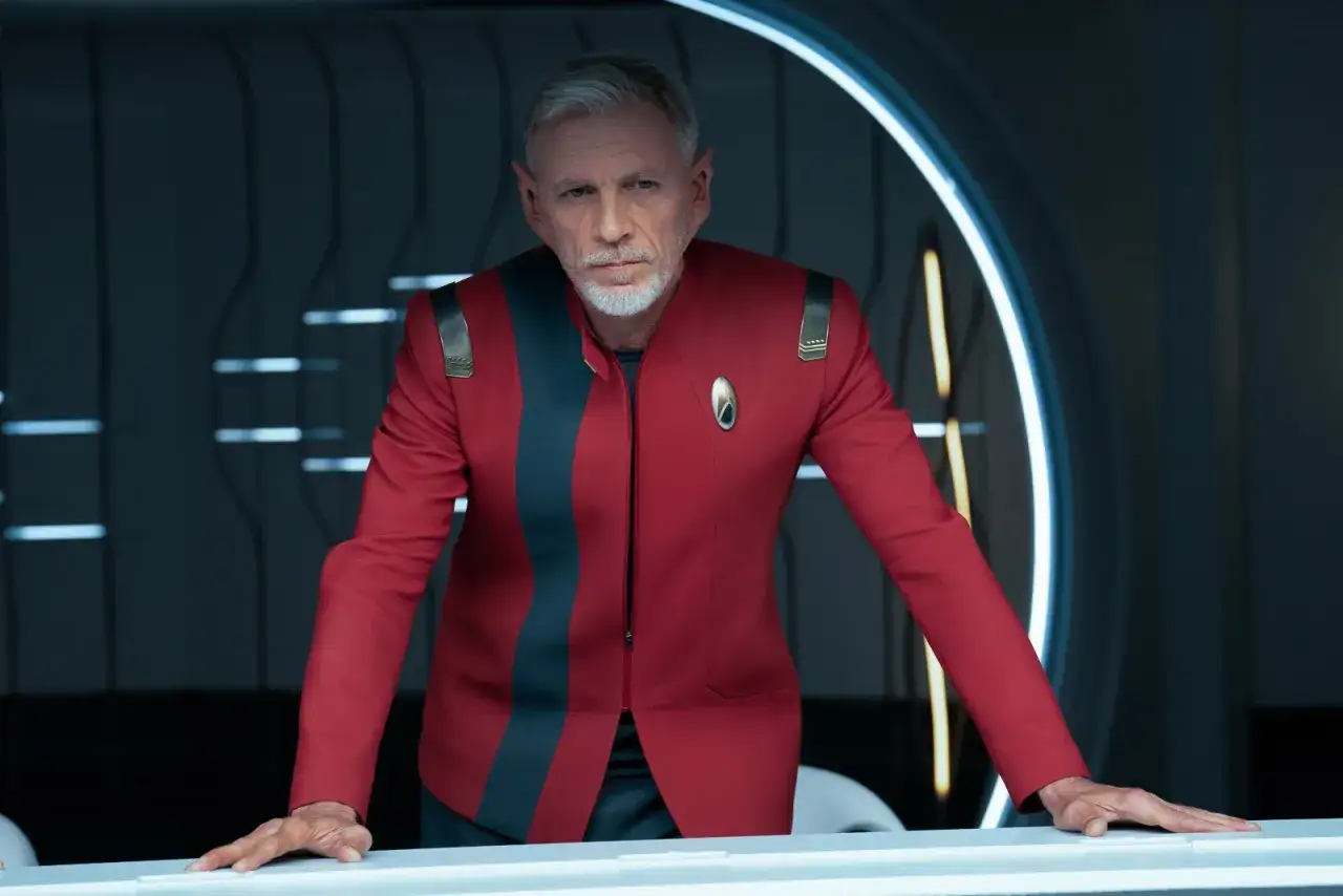Starszy mężczyzna z siwymi włosami i spiczastymi uszami w czerwonym mundurze. To część obsady Star Trek Discovery.