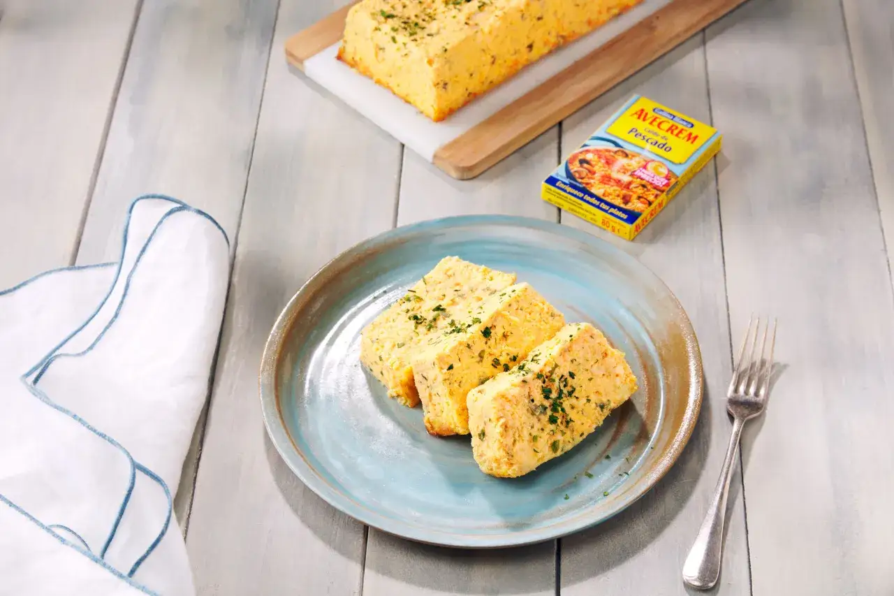 Pastel de pescado al horno, cortado en porciones y servido en plato azul. Un trozo entero reposa sobre tabla de madera.