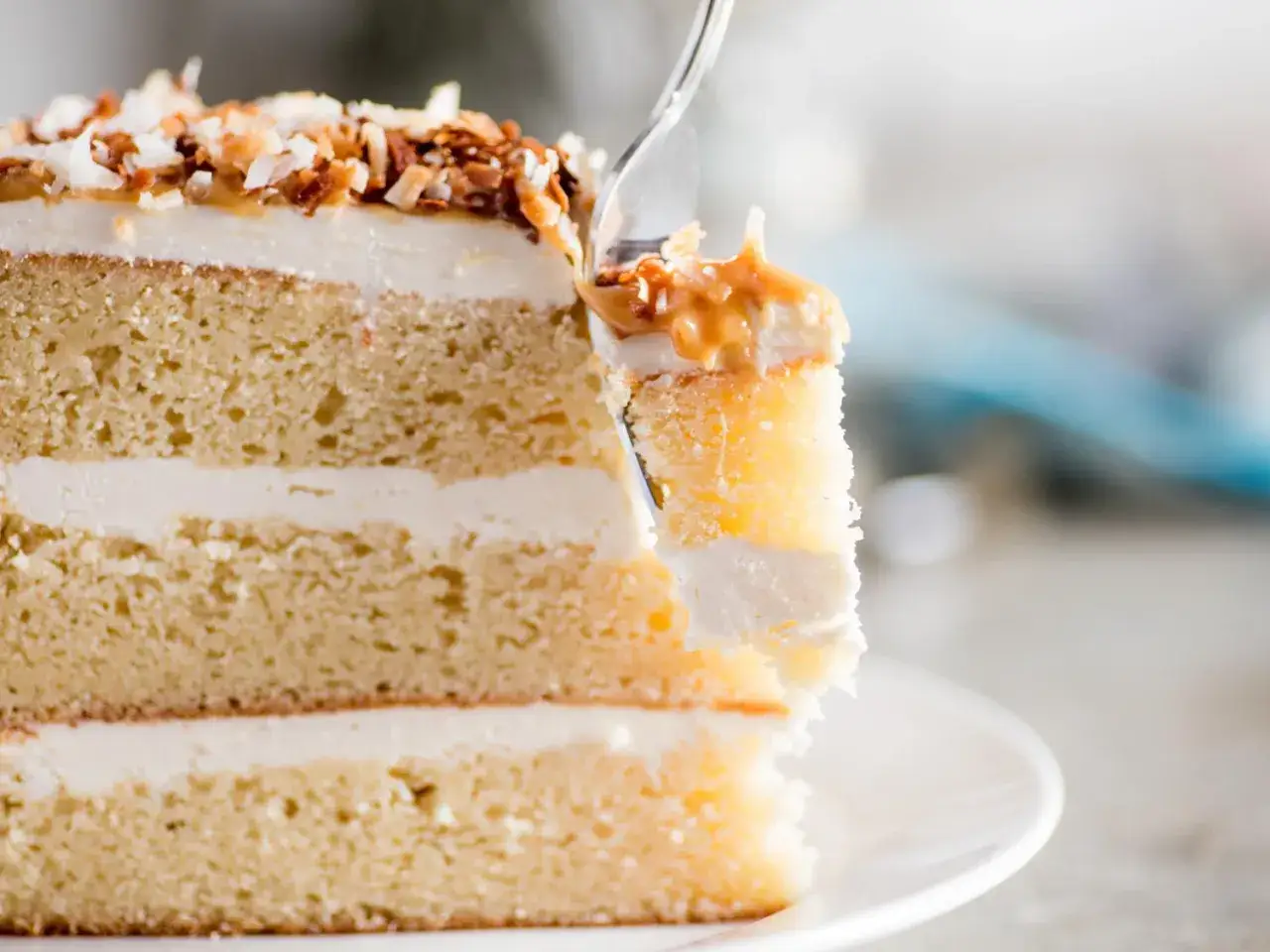 Une part de g&acirc;teau moelleux aux couches de cr&egrave;me noix de coco, garnie de noix de coco grill&eacute;e et de caramel.