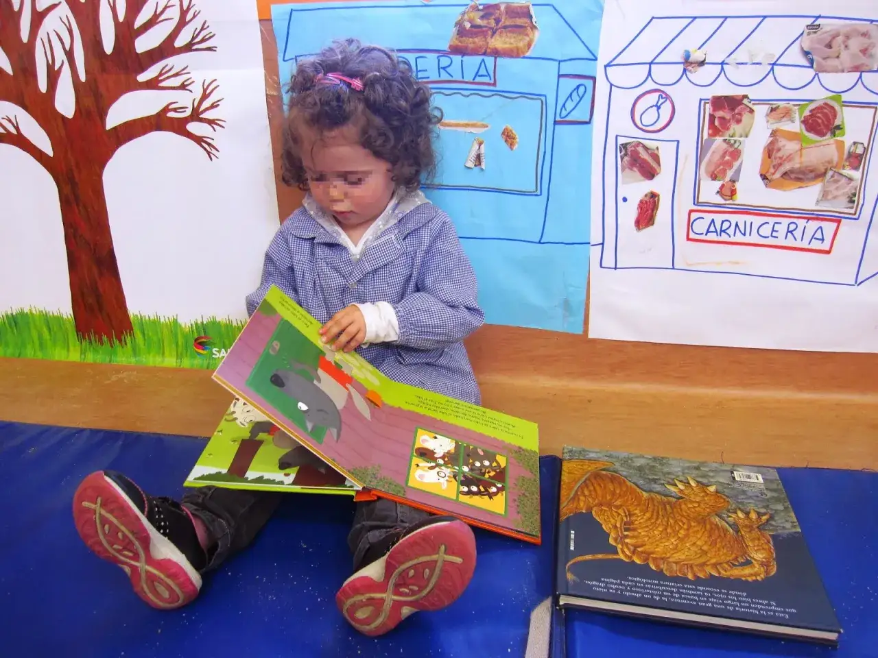 Ni&ntilde;a con rizos lee un cuento sobre un lobo y conejos. Detr&aacute;s, un dibujo de una carnicer&iacute;a.