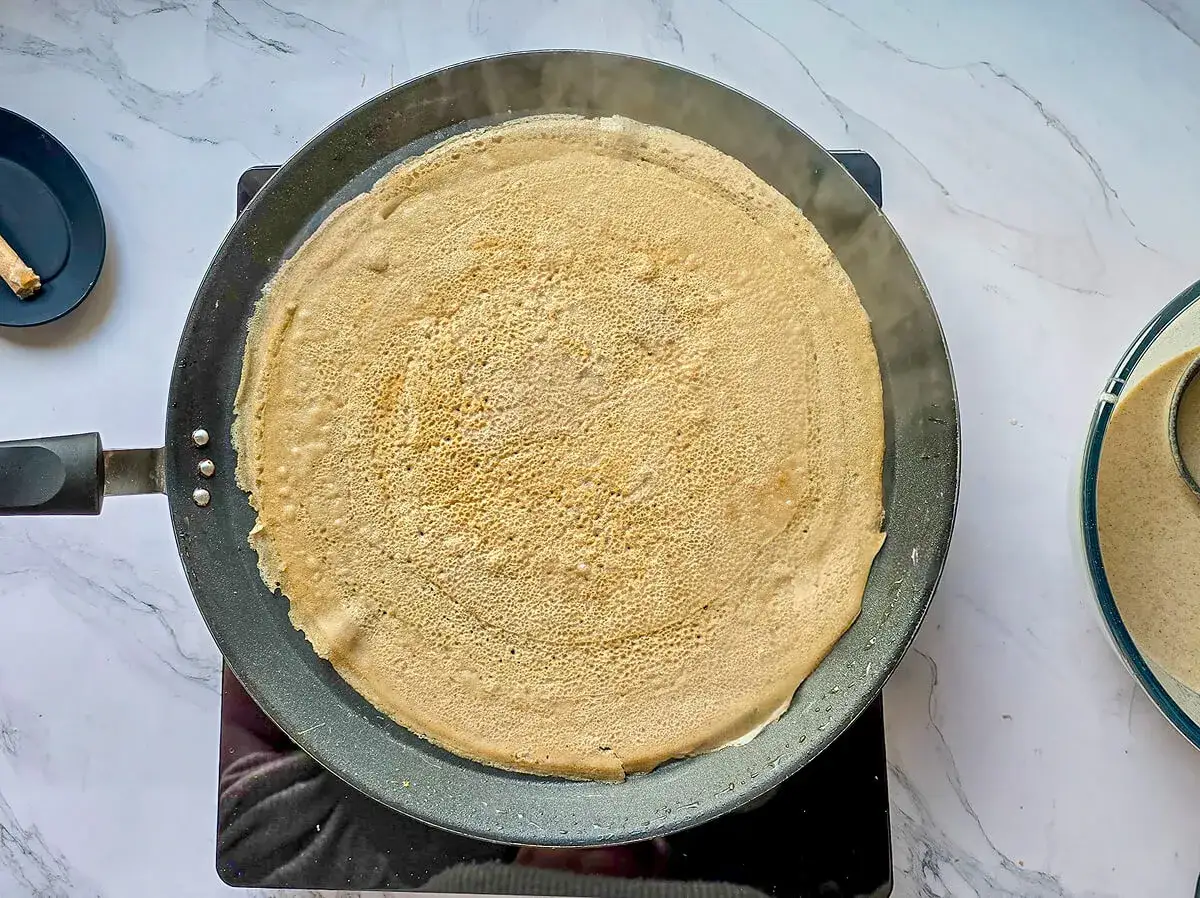 Une crêpe dorée cuit dans une poêle, prête pour une délicieuse recette de pâte à crêpes.