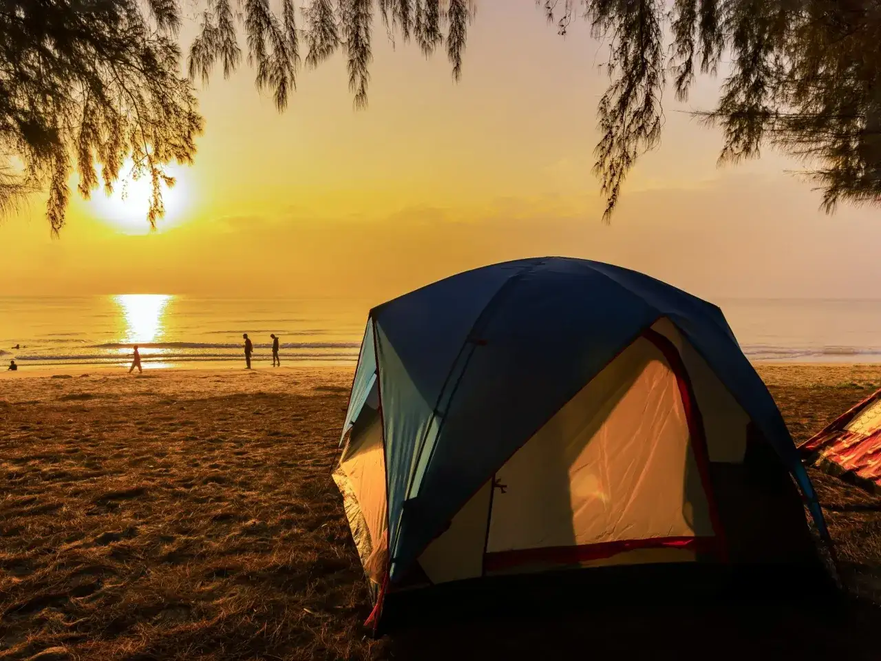 Namiot na plaży o zachodzie słońca. Widok na morze i sylwetki ludzi. To z pewnością jedne z najpiękniejszych pól namiotowych w Polsce.