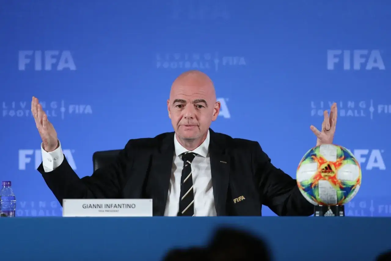 Prezydent FIFA, Gianni Infantino, gestykuluje podczas konferencji prasowej obok piłki nożnej.