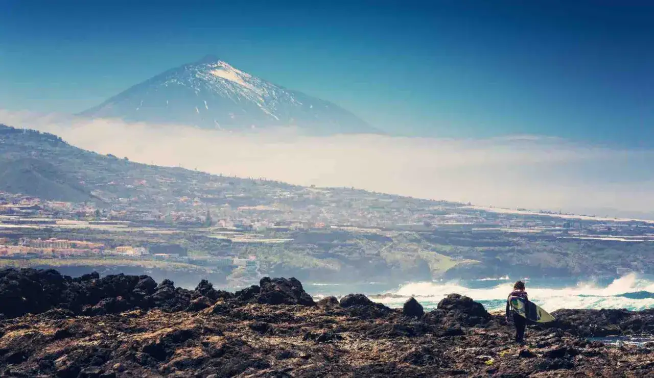 Surferin blickt auf das Meer, im Hintergrund der schneebedeckte Teide. Ein typischer Anblick auf Teneriffa im Dezember.