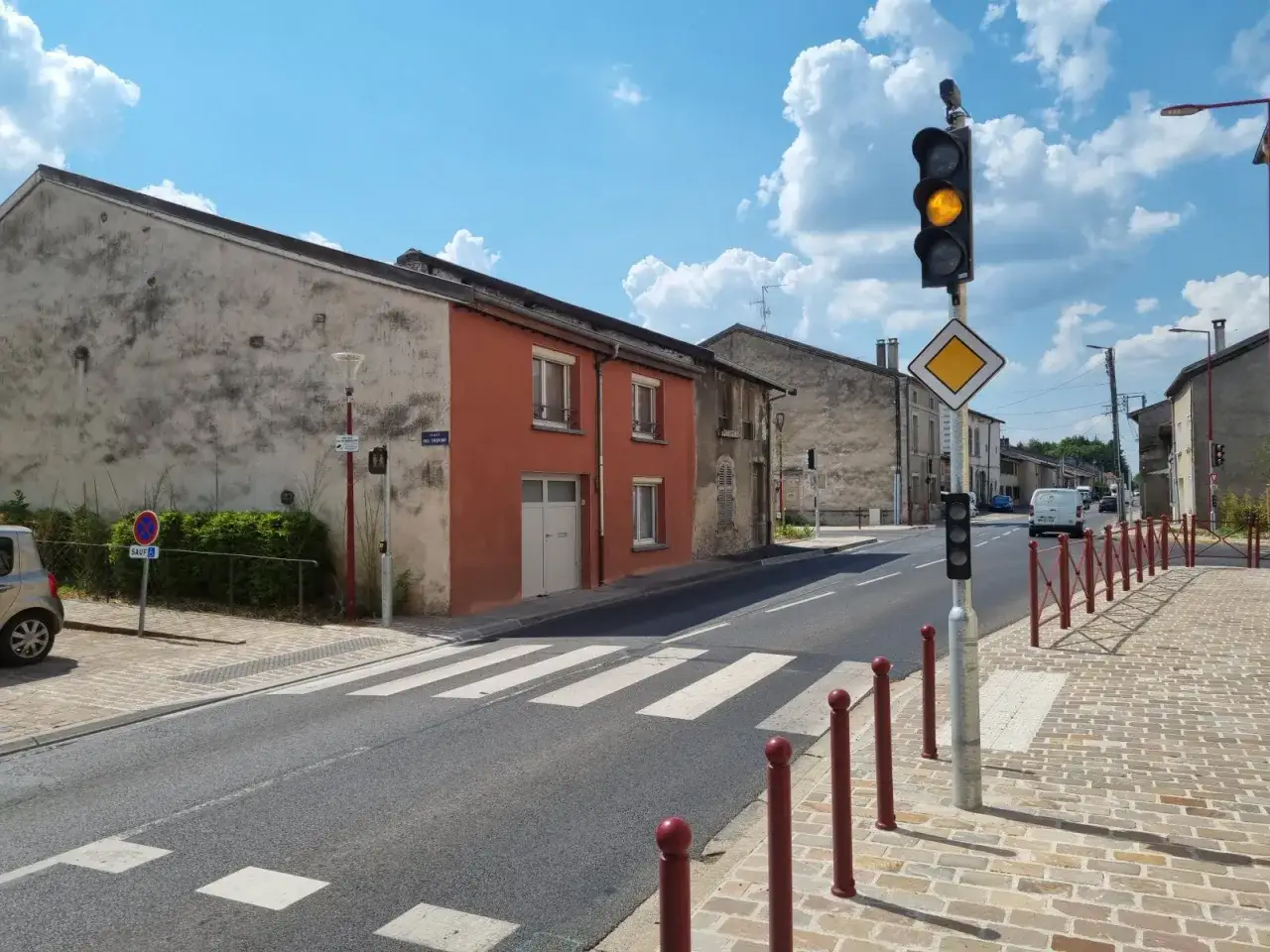 Un feu de signalisation avec un feu orange clignotant en bas, sur une rue avec passage piéton et maisons.
