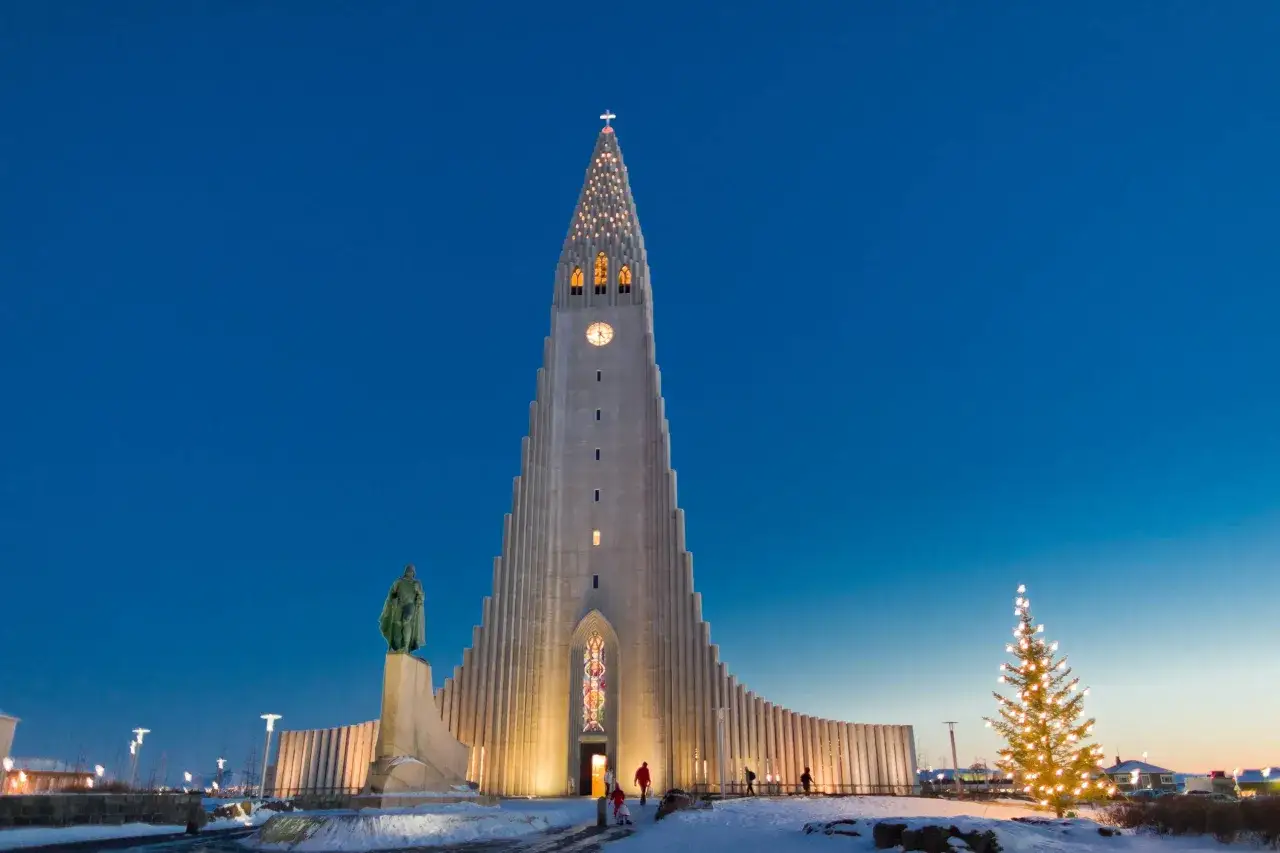 Hallgr&iacute;mskirkja w Reykjaviku, Islandia, nocą. Oświetlona świątynia z pomnikiem przed nią i choinką.