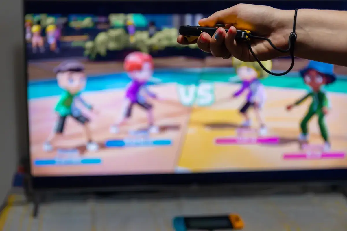 Ręka trzymająca kontroler do gier Nintendo Switch, na ekranie kolorowe postacie w grze ruchowej.