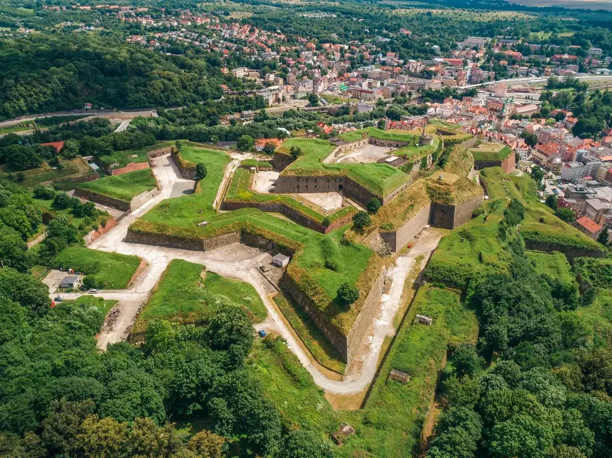 Imponująca twierdza w Kłodzku, jedna z największych atrakcji regionu, rozpościera się na wzgórzu, otoczona zielenią i miastem.