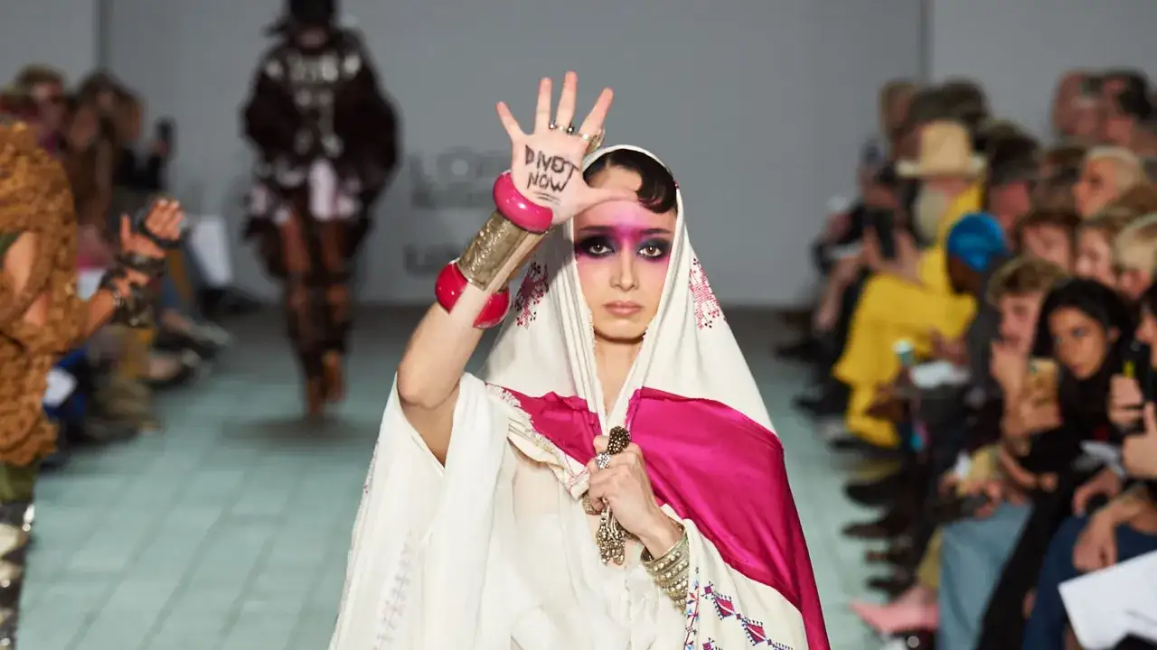 A model on a runway, showcasing designs by Palestinian designers, holds up her hand with