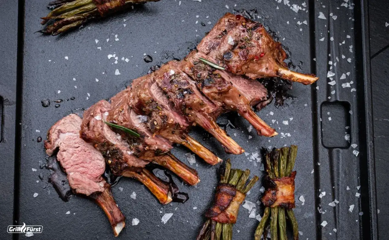 Ein saftiges Lammkarree, perfekt gegrillt, mit Rosmarin und Gew&uuml;rzen verfeinert, daneben Spargelb&uuml;ndchen im Speckmantel.