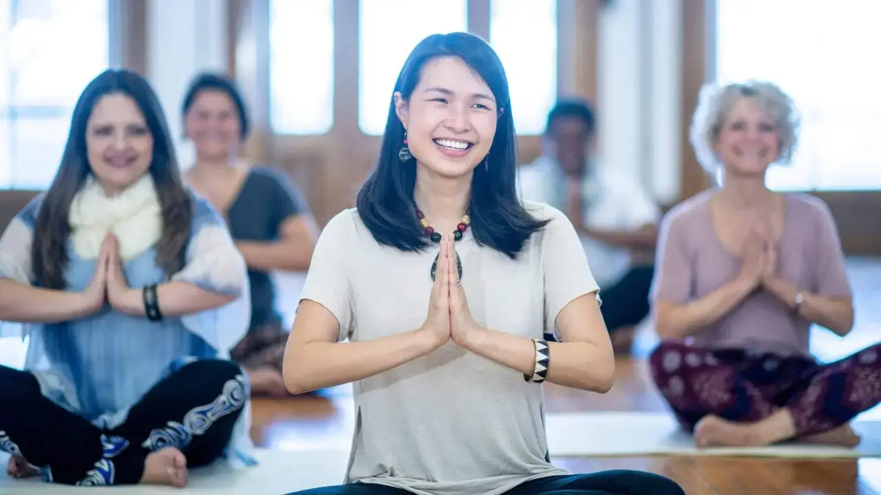 En grupp m&auml;nniskor sitter i lotusst&auml;llning och ler under en kundalini yoga-klass.