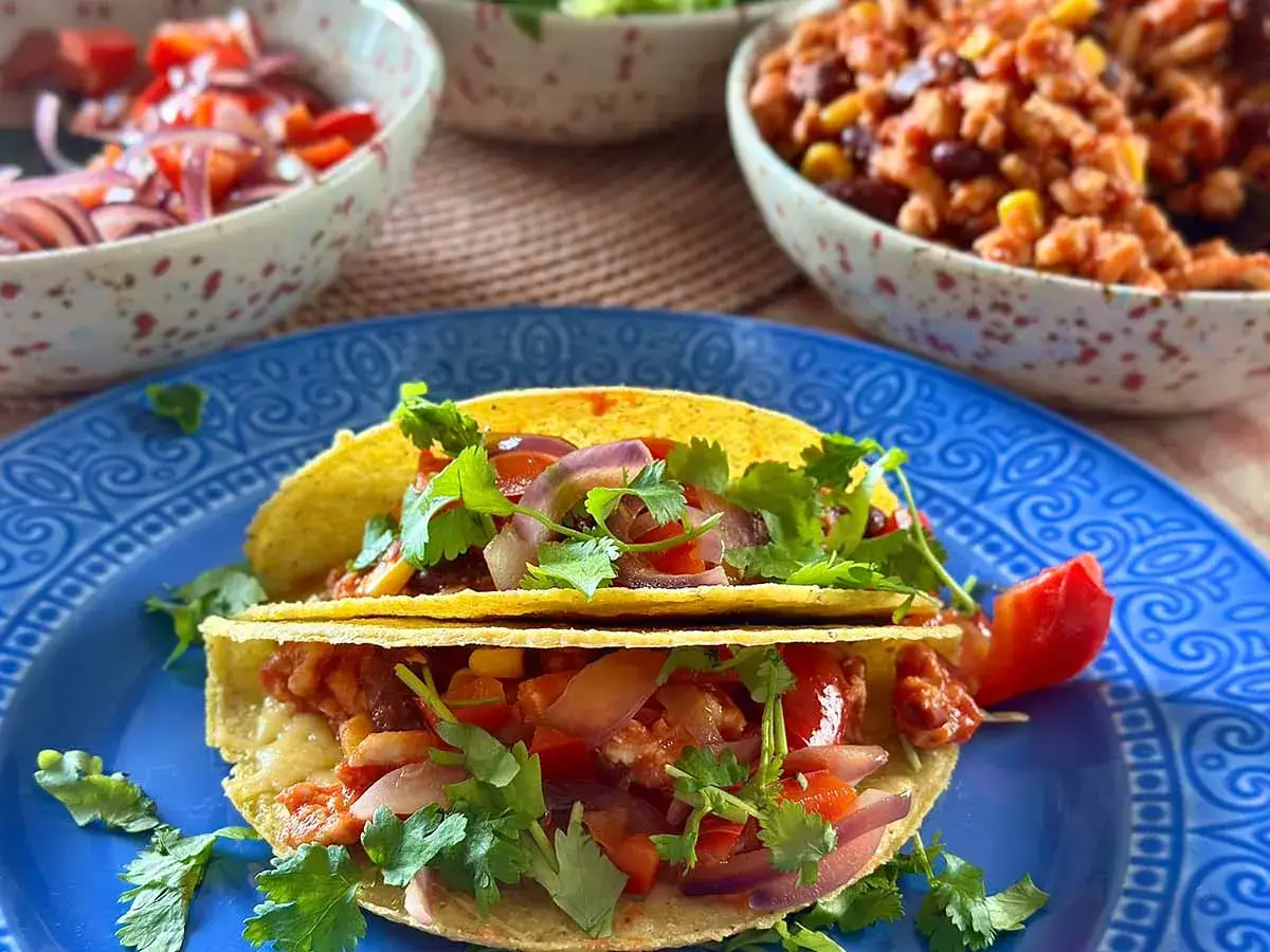 Gotowe Tacos przepis: chrupiące muszelki wypełnione mięsem mielonym, fasolą, kukurydzą, pomidorami i czerwoną cebulą, posypane świeżą kolendrą.