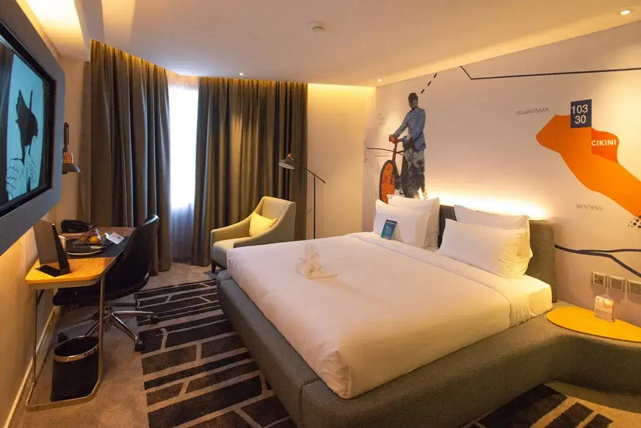 Nowoczesny pokój hotelowy z dużym łóżkiem, biurkiem i fotelem. Na ścianie mural z mapą. Idealne miejsce, gdzie najlepiej rezerwować noclegi.