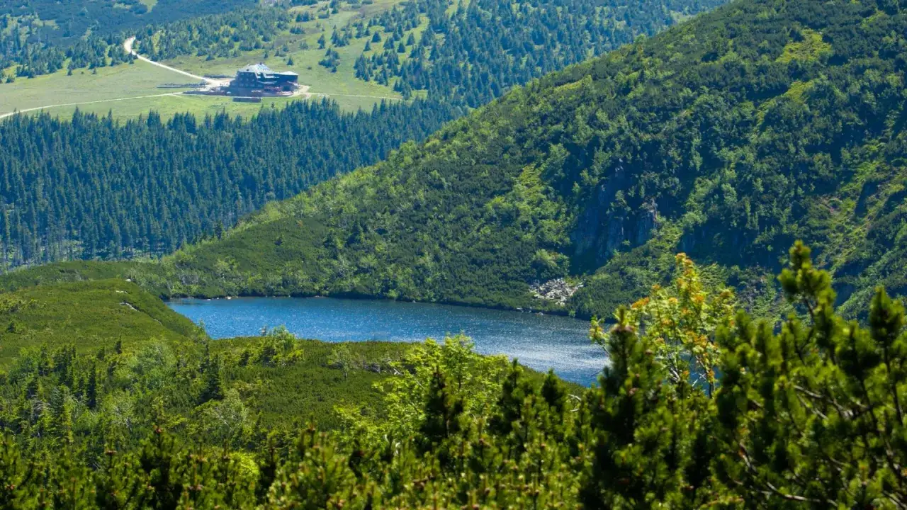 Widok na górskie jezioro i schronisko Samotnia w Karpaczu, otoczone zielonymi lasami i zboczami.