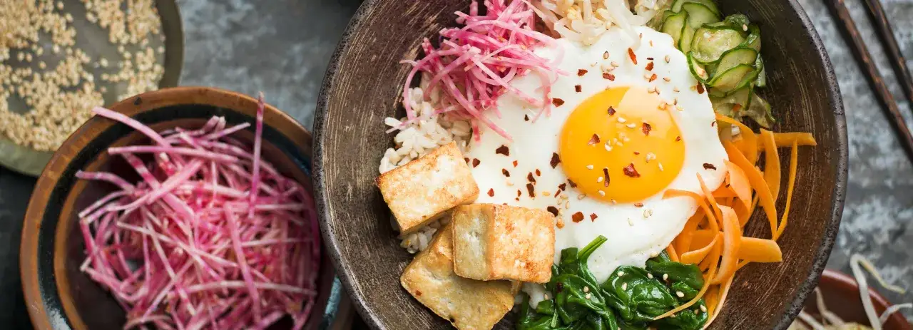 En skål med bibimbap, ris, stekt ägg, tofu och grönsaker. Perfekt vin till koreansk mat.