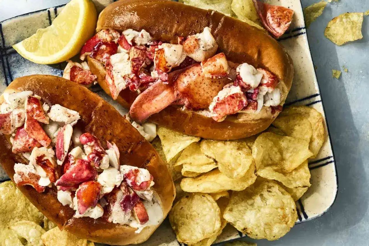 Deux sandwichs hummer généreusement garnis de homard, accompagnés de croustilles dorées et d'un quartier de citron.