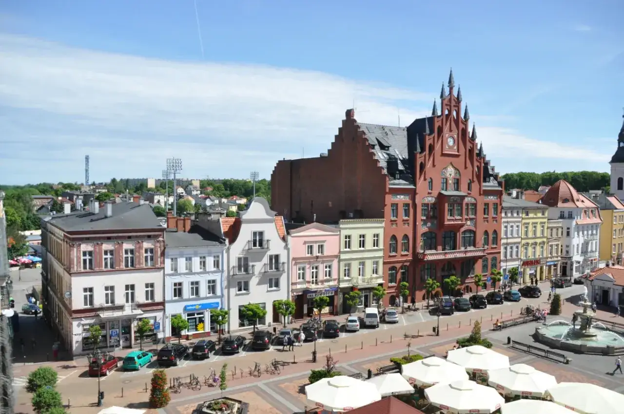 Kolorowe kamienice w Lipienicach tworzą malowniczy rynek. Słońce odbija się od dachów, a fontanna dodaje uroku.